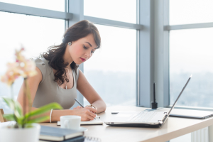 Work day of busy office manager, writing business plan in her notebook, working at work table.